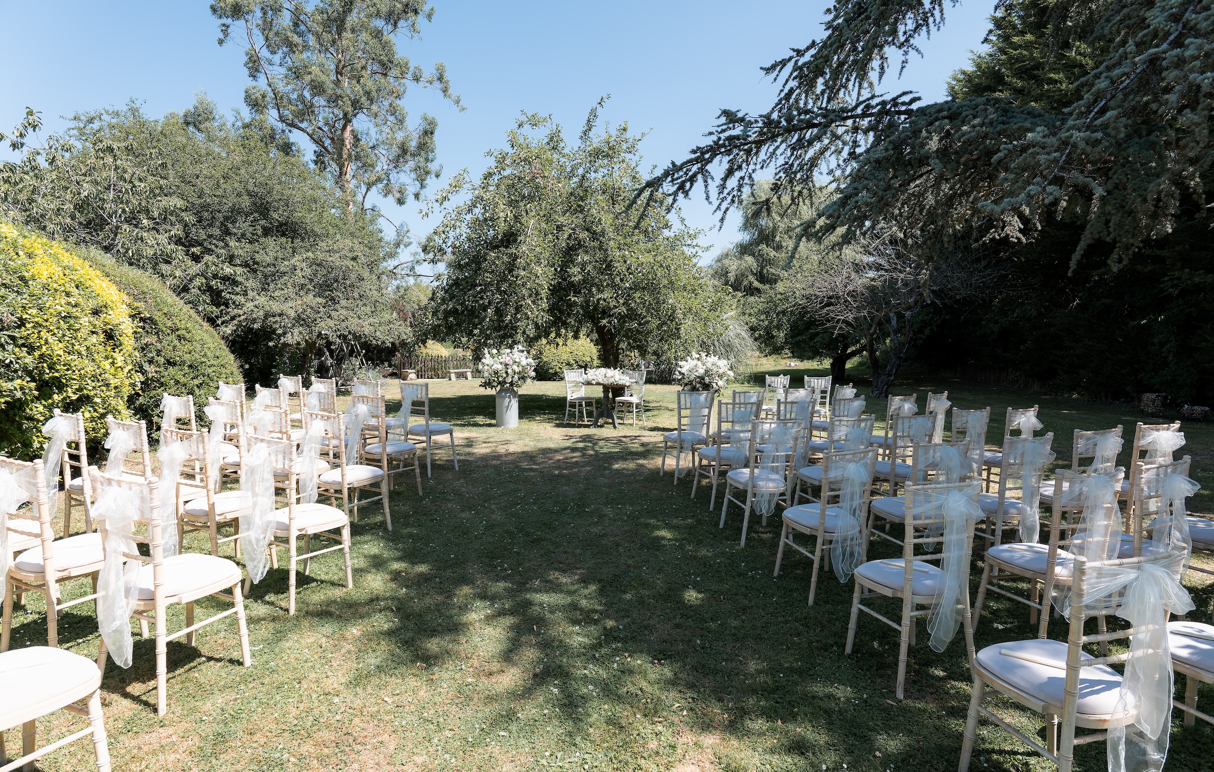 Rows of white wedding chairs and flowers arranged for Laura and Ross’s outdoor ceremony in the gardens at Widbrook Grange.