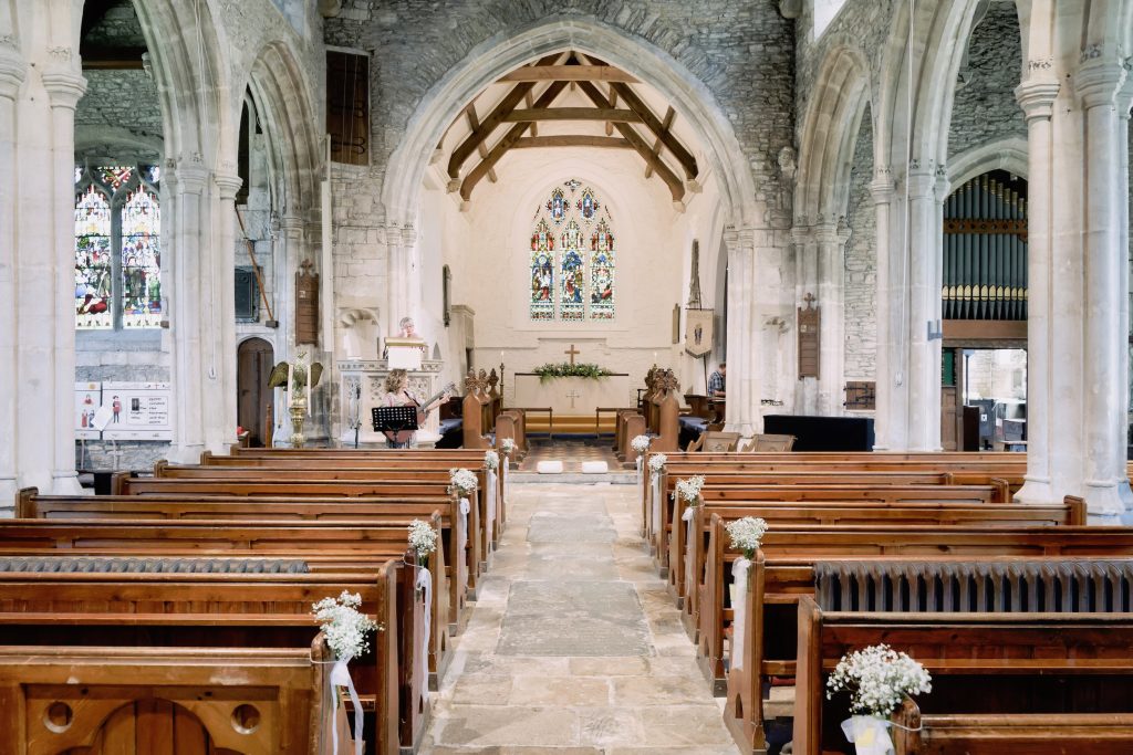 The stone aisle, wooden pews and flower decorations inside St George’s Church in Beckington before Alice and Ben’s wedding.