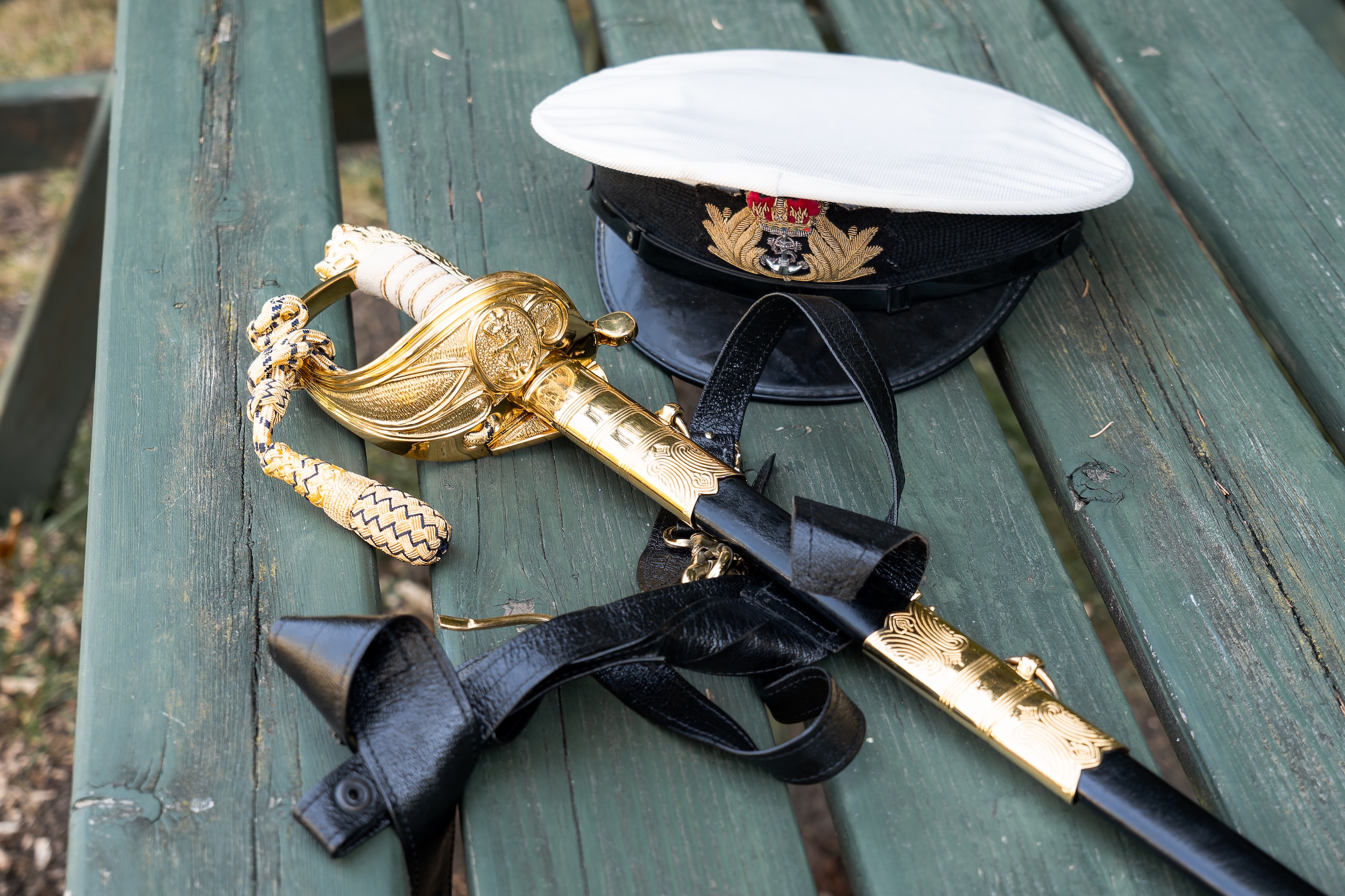 A military dress sword and white peaked cap laid on a weathered green wooden bench before Laura and Ross’s wedding.