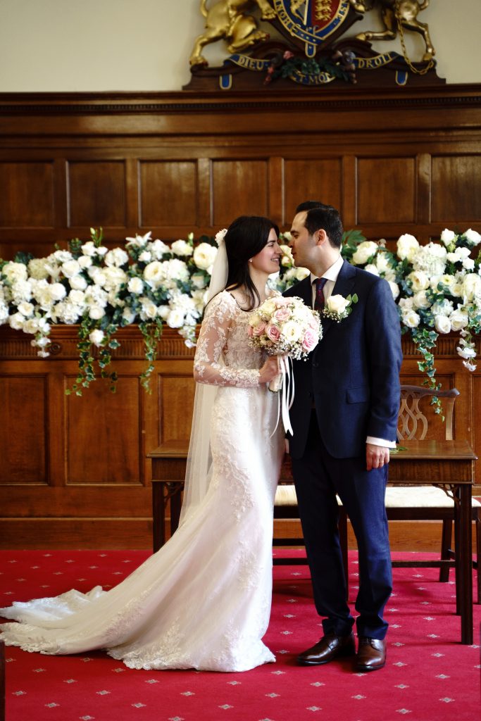 Habibi and Elaina leaning towards one another in the wood-panelled ceremony room at Bath Guildhall.