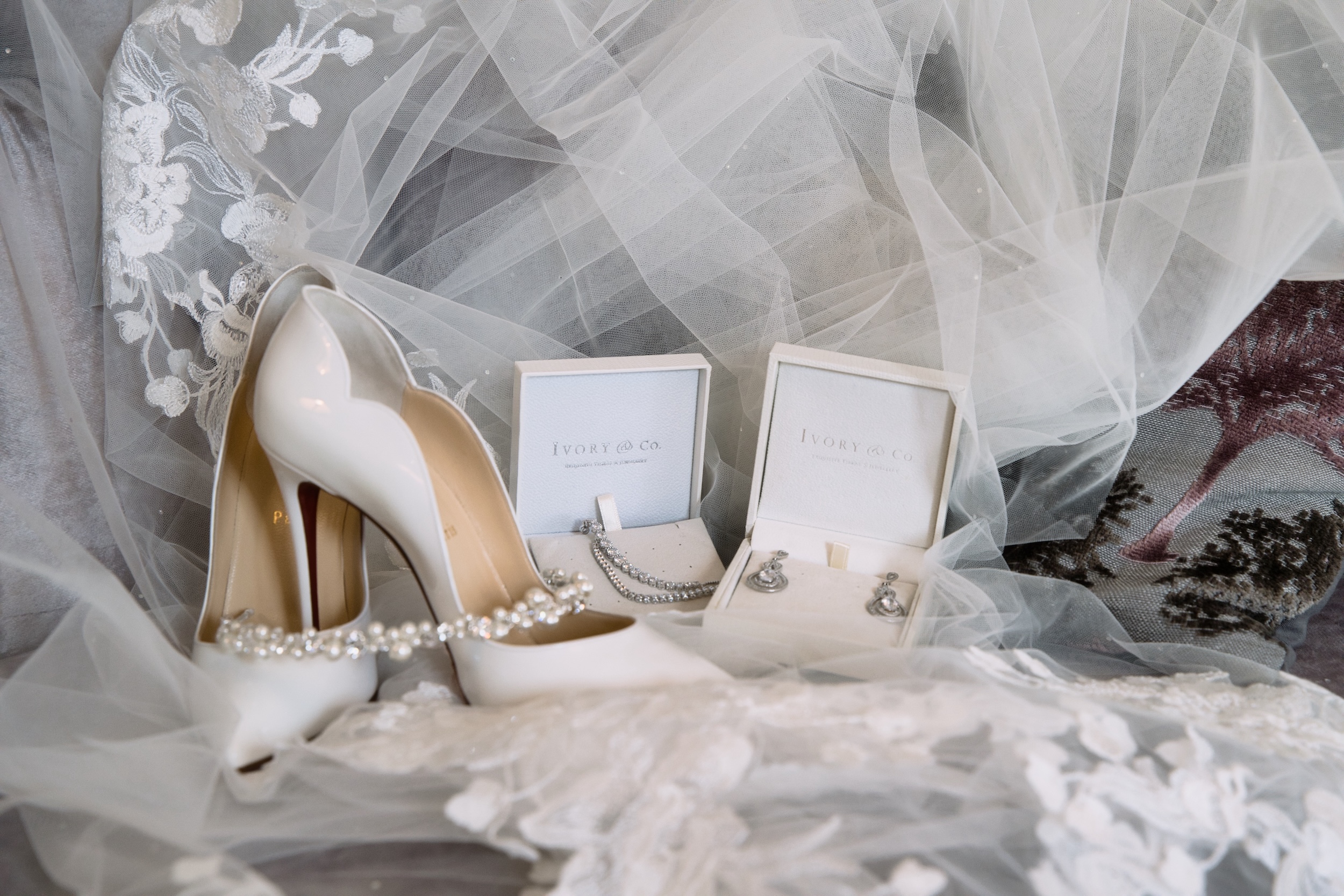 White bridal shoes with pearl details beside jewellery boxes and a lace-edged veil before Katie and Jack’s wedding.