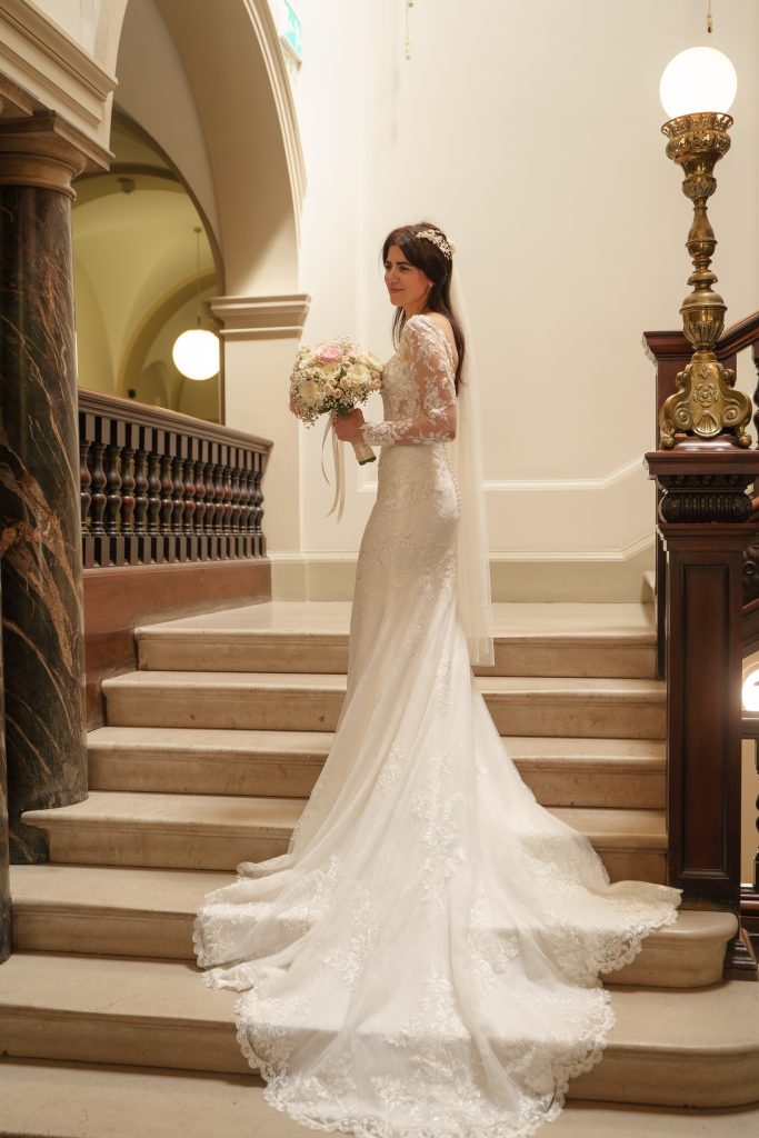 Elaina holding her bouquet on the stone staircase at Bath Guildhall, with her lace train spread across the steps.