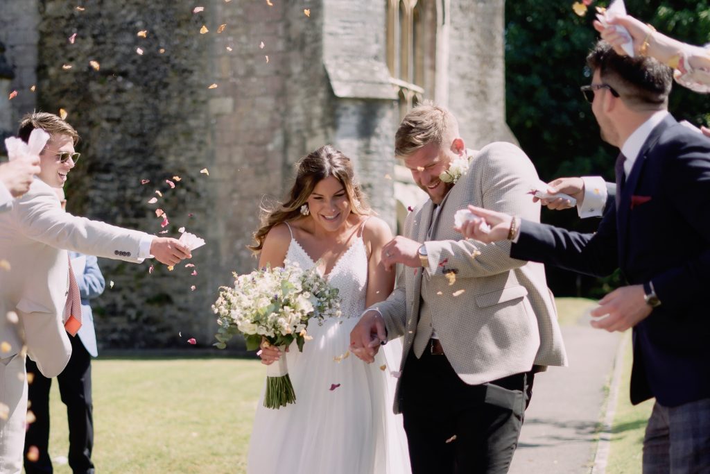 Alice and Ben walking through confetti outside St George’s Church in Beckington before their Seymours Court reception.