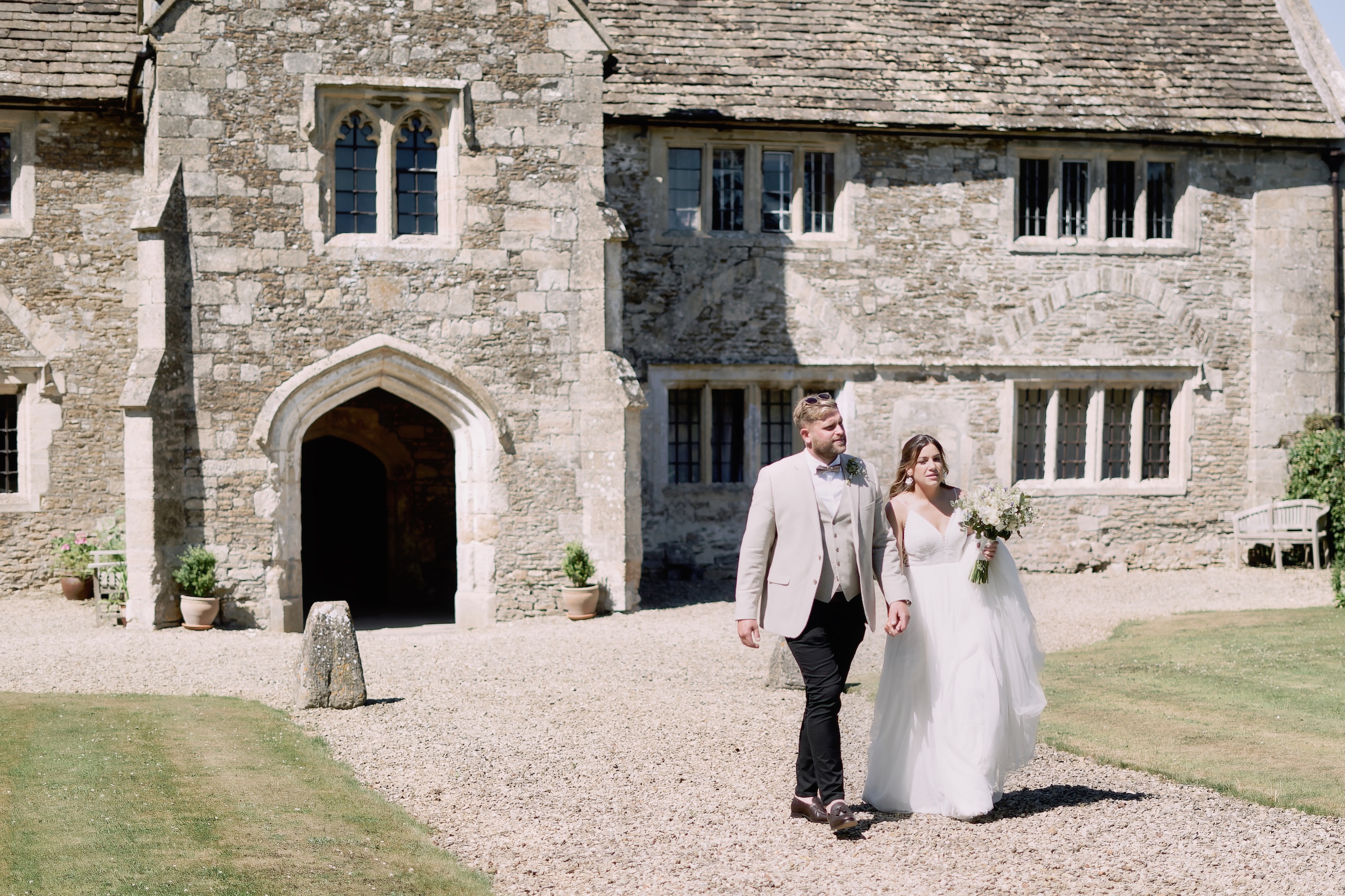 Alice and Ben walking hand in hand in front of the stone manor house at Seymours Court, Beckington.