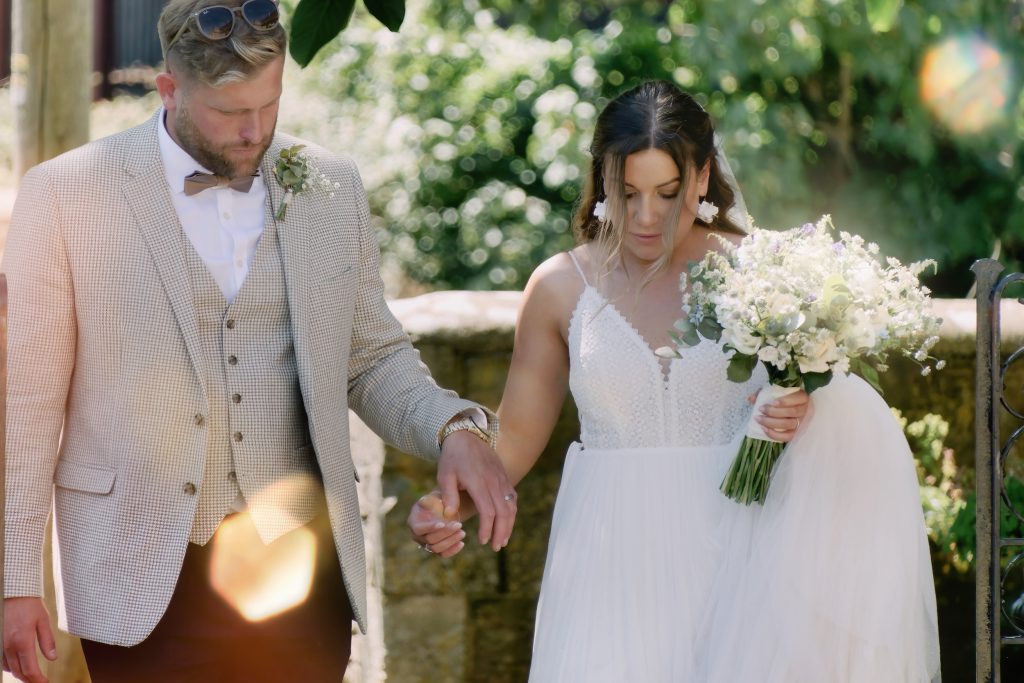 Alice and Ben holding hands in the summer sunshine during a few relaxed wedding portraits.