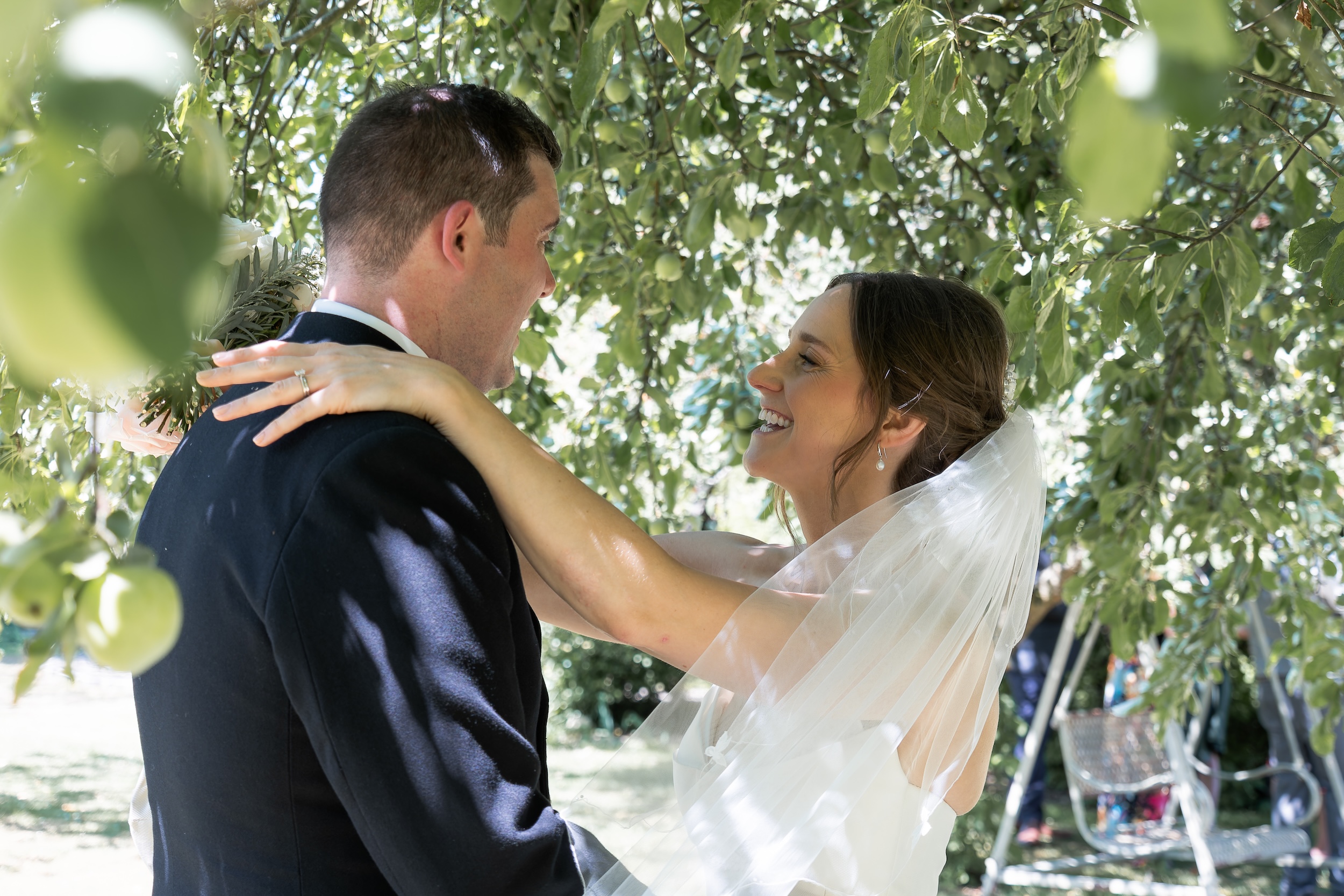Laura smiling at Ross with her arms around his shoulders beneath leafy branches at Widbrook Grange.